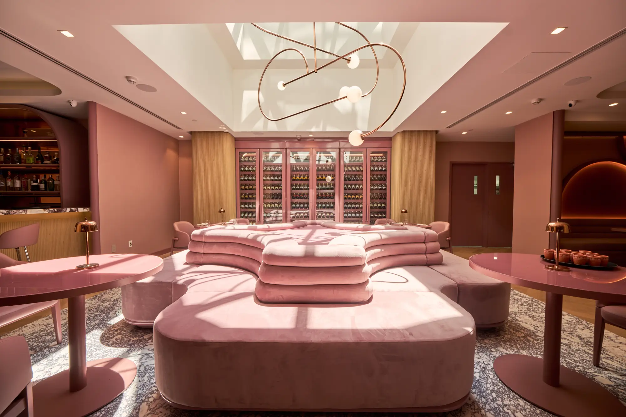 blush-toned lounge with a curved banquette and glass-fronted wine cabinets