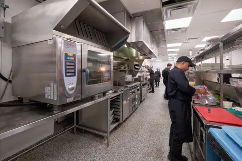 combi oven on a stainless stand beside the cook line with a chef working