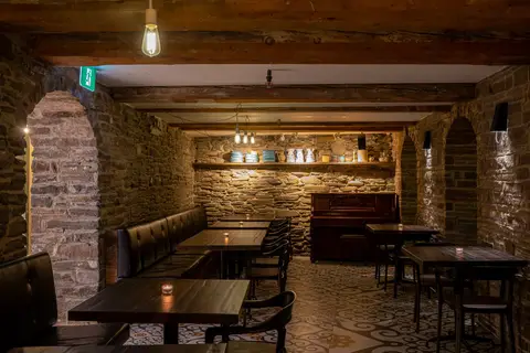 back dining room with an upright piano against a stone wall