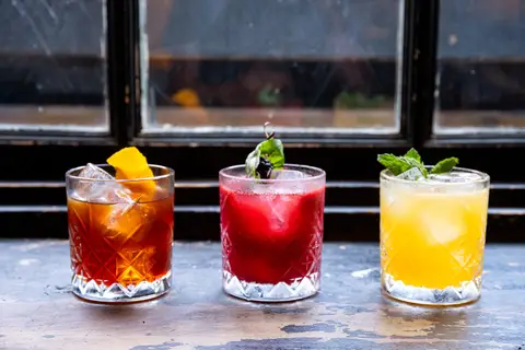 three cocktails on a ledge in front of a window