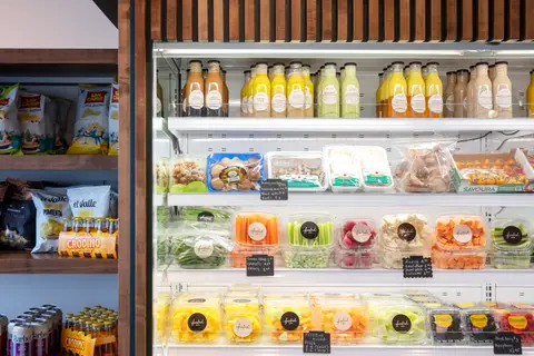 refrigerated case of cut fruit and vegetables beside packaged snacks