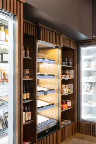walnut shelving with dry goods beside a glass-door refrigerator