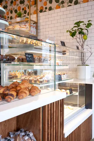 bakery case with croissants and cakes against a tiled wall